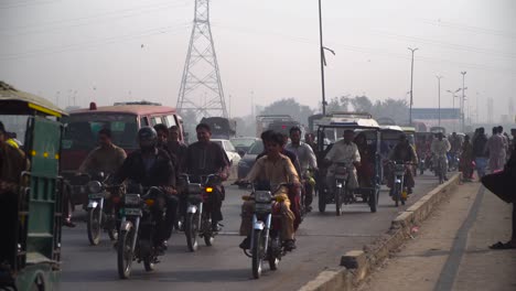 Traffic-going-on-the-bridge-under-the-fly-over,-A-passenger-bus-top`s-full-of-luggage,-motor-bikes-and-cars,-cycle,-Buses,-rickshaw`s-passing,-electric-polls-and-satellite-towers-in-the-background