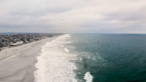 Aerial-flyover-of-the-a-small-barrier-island-beach-town-along-the-coast-as-waves-crash-into-the-shore