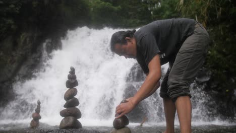 Hombres-Construyendo-Esculturas-Rocosas-De-Cairns-En-Un-Río-Caudaloso-Para-Relajarse