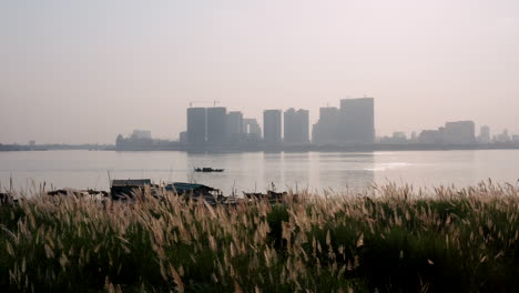 Aerial-drone-footage-from-down-to-up-revealing-a-fisherman-floating-house-on-the-Mekong-shore-with-Phnom-Penh-panorama-on-the-background