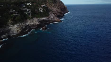 Drone-shot-of-a-cliffside-beach-that-has-both-amazing-houses-and-a-nice-views-of-the-waves-crashing-on-the-smoothed-out-cliffs