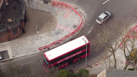 Aerial-tracking-shot-of-a-famous-red-London-bus,-traveling-towards-Surbiton-train-station-on-the-Suburbs-of-London,-UK