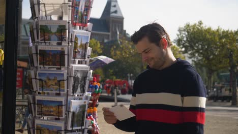 Charming-young-man-looking-at-postcards-on-a-tourist-trend-market-in-Amsterdam