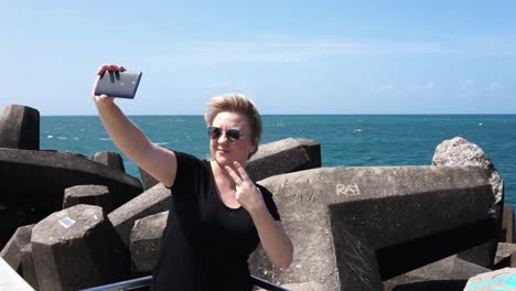 Mujer-Joven-Tomando-Un-Selfie-En-El-Teléfono-Celular-En-El-Muelle-Con-El-Océano-En-El-Fondo