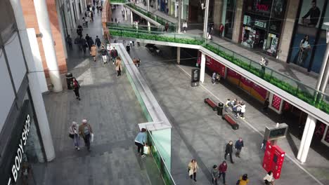 High-angle-perspective-view-down-to-shoppers-in-slow-motion-in-busy-city-shopping-mall,-retail-district