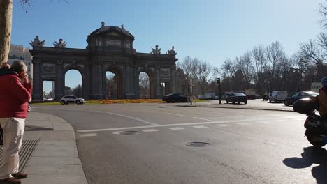 Daytime-traffic-in-front-of-Puerta-de-Alcalá-at-Plaza-de-la-Independencia-in-Madrid,-spring-summer