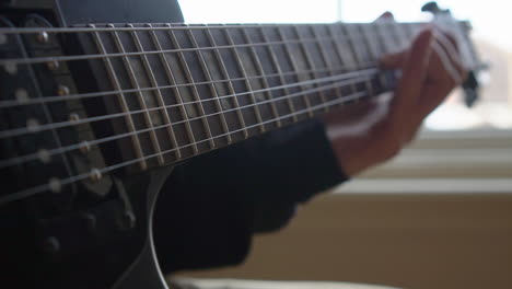 Man-Practising-a-vintage-black-electric-guitar,-rehearsing-chords,-solos-and-octaves-in-a-natural-light-environment.