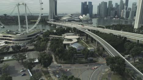 Flying-over-to-Singapor-city-center-with-all-attractions-and-famous-buildings,-like-marina-bay-sands,-helix-bridge,-merlion,-ferris-wheel,-cars-traffic-by