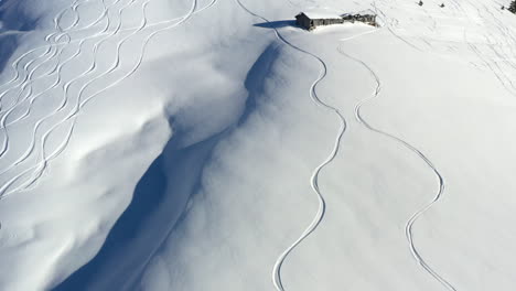 Luftaufnahme,-Die-Nach-Oben-Zeigt,-Um-Frische-Skispuren-Im-Neuschnee-Zu-Zeigen,-Und-Dann-Den-Blick-Auf-Eine-Alte-Berghütte-–-Scheune-–-Am-Hang-Eines-Hügels-Freigibt