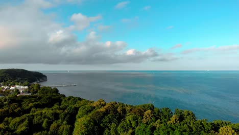 Beautiful-blue-sea,-clouds-over-blue-sea,-slow-flight-over-trees-overlooking-the-bay,-smooth-aerial-shoot