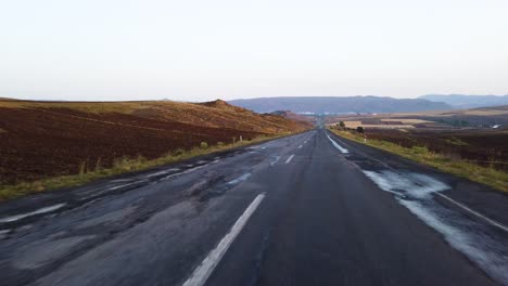 View-from-inside-car-on-empty-hilly-road-leading-to-horizon-line-at-sunset-or-sunrise