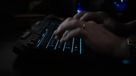 Side-view-of-a-cyber-criminal's-hands-typing-on-a-backlit-keyboard,-dark-office