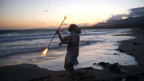 Un-Bailarín-De-Arte-De-Flujo-Masculino-En-Silueta-Interpretando-Su-Fuego-Girando-En-La-Playa-Al-Atardecer-Con-Olas-Oceánicas-En-Cámara-Lenta