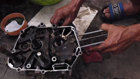 Mecánico-Se-Agacha-En-El-Pavimento-Para-Reparar-Las-Piezas-Del-Motor-De-Uno-De-Los-Millones-De-Motonetas-En-La-Ciudad-De-Ho-Chi-Minh,-Vietnam