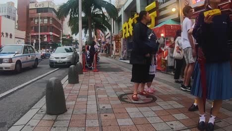Pedestrians-loitering-outside-eateries-along-Kokusai-dori,-popular-shopping-street,-Naha,-Okinawa