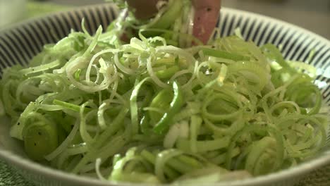 EXTREME-CLOSE-UP-Male-chef-mixing-sliced-leeks-with-oil,-salt-and-pepper