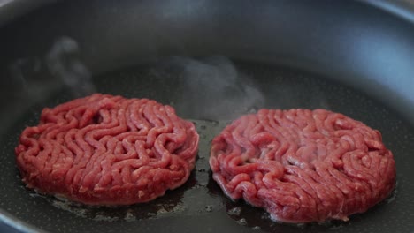 Two-raw-ground-beef-steaks-cooking-on-electric-pan,-close-up-still-shot