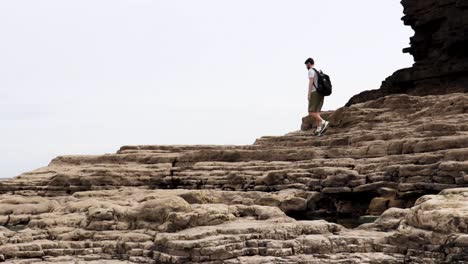 A-young-man-walking-across-some-large-rocks-on-a-beach
