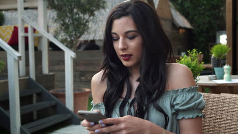 Confident-and-attractive-young-brunette-woman-in-a-casual-top,-uses-her-cellphone,-smiles-happily-to-the-text-messages,-looks-around-with-a-stylish-outfit