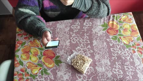 white-woman-eating-peanuts-on-a-table-and-using-cell-phone
