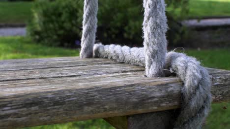 CLOSE-UP-view-of-wooden-swing-seat-gently-swaying-in-the-wind-hung-by-rope