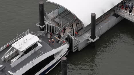 Commuters-boarding-NYC-Ferry-on-a-rainy-morning-at-Long-Island-City,-New-York,-filmed-from-above