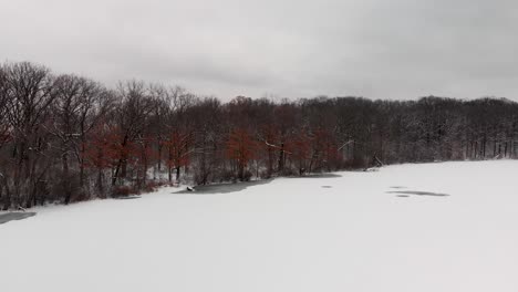 aerial-drone-pan-shot-frozen-lake-and-snow-covered-in-trees-in-forest-4k