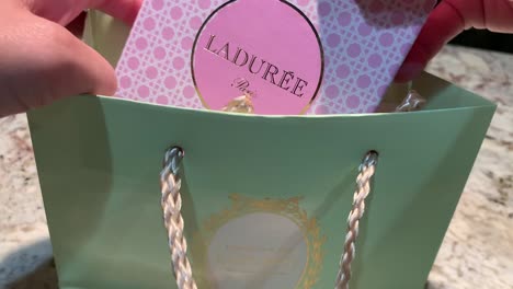 A-female-hand-opening-up-a-specialty-gift-bag-and-box-from-the-famous---Laduree-Paris-bakery