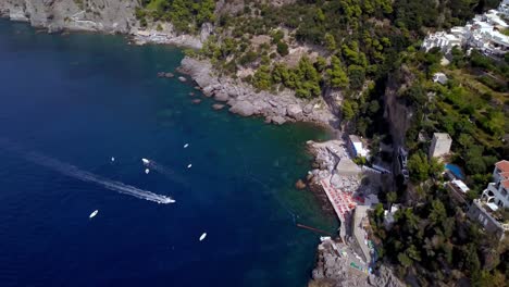 The-Praiano-Lido-One-Fire-Beach-near-Positano-Italy-with-homes,-boats-and-hotels-on-the-cliffside,-Aerial-orbit-reveal-shot