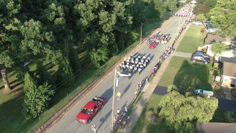 Tilt-down-aerial-of-marching-band-in-Fourth-of-July-parade,-US-flag-with-Boy-Scouts-following