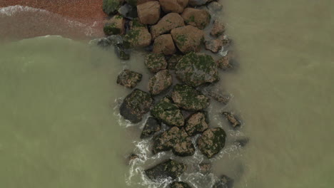 Aerial-top-down-view-of-breakwater-hitting-rocks-on-the-coastline,-on-the-south-coast-of-England,-starting-close-and-rising-up