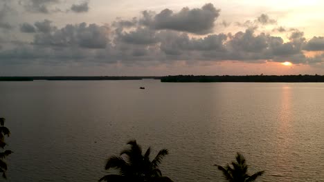 Beautiful-aerial-shot-of-a-backwater-Vembanadu-Lake,water-lines,twilight-sunset,coconut-trees-,water-transportation,clouds,reflation,House-boat,red-sun