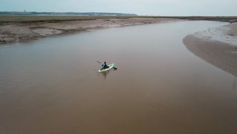 Man-kayaking-on-meandering-river,-drone-pans-round-kayaker