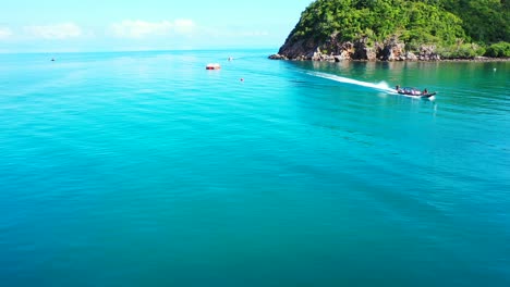 Fishing-boat-sailing-on-calm-azure-lagoon-alongside-beautiful-shore-of-tropical-island-with-rocky-coastline-and-lush-vegetation-in-Vietnam