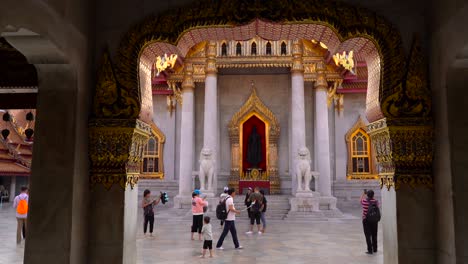 Bangkok-Thailand-Wat-Benchamabophit-Temple-Facade-Showing-Buddha-Statue-Mounted-On-The-Wall-With-Golden-Edge-Frame-Alongside-Are-Two-Marble-Sculptured-Lion-Images---Medium-Shot