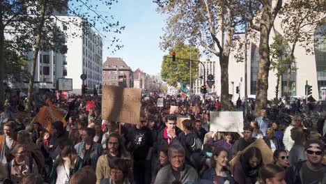 Friendly-crowd-of-protsters-of-all-ages-march-down-a-street-in-Cologne,-Germany,-holding-posters-and-banners,-to-demand-political-action-against-climate-change