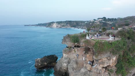 Tourists-and-Wedding-Couple-on-Cliff-On-Bali-Island,-Pull-Back-Aerial