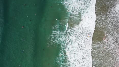 Praia-da-Arrifana-in-west-Portugal-with-Surfers-seen-from-above-riding-waves,-Aerial-top-view-rotating-shot