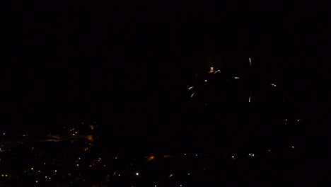Celebration-with-colorful-and-sparkling-fireworks,-over-a-mountain-town,-at-night