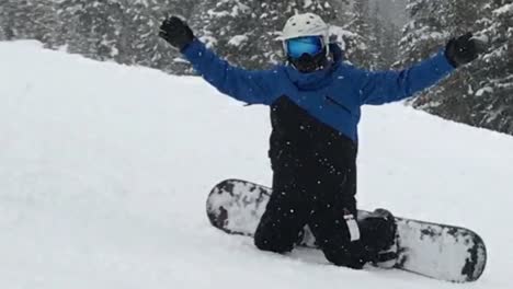 Slow-motion-a-triumphant-snowboarder-kneels-in-the-fresh-powder-as-the-snow-falls-down-around-him,-Powder-Mountain,-Utah