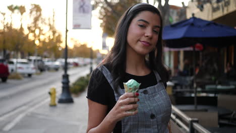 Adult-hispanic-woman-eating-a-messy,-dripping-ice-cream-cone-dessert-on-the-city-street-at-sunset-SLOW-MOTION