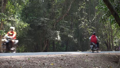 Toma-Exterior-Mediana-Del-Tráfico-Que-Pasa-Por-Una-Carretera-Rural-Con-Un-Telón-De-Fondo-Selvático-En-La-Carretera-A-Angkor-Wat