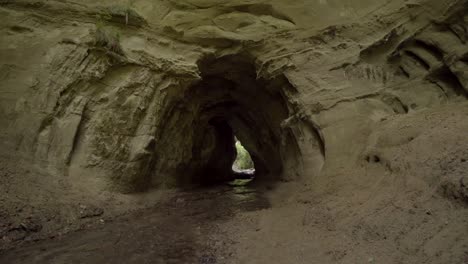 Pan-shot-of-river-flowing-through-a-sandy-cave-hole-outdoors-in-nature