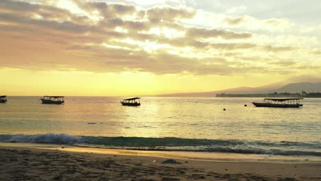 Goldener-Sonnenuntergang-Mit-Leuchtend-Gelbem-Himmel-Und-Grauen-Wolken,-Die-Sich-Auf-Dem-Ruhigen-Meer-Spiegeln,-Mit-Booten,-Die-In-Der-Nähe-Des-Strandes-In-Indonesien-Schwimmen