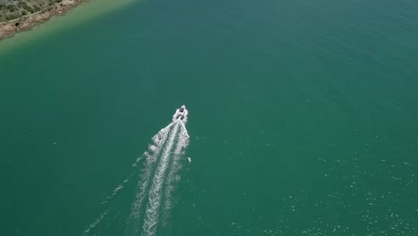 Motorboat-crossing-lagoon-navigates-deep-channel-near-shore,-aerial