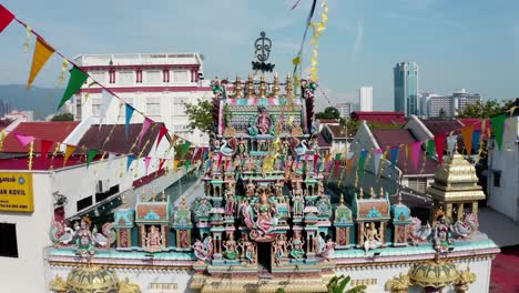Front-facade-of-Sri-Mariamman-Hindu-Temple-with-prayer-flags-and-deity-sculptures,-Aerial-drone-approach-shot