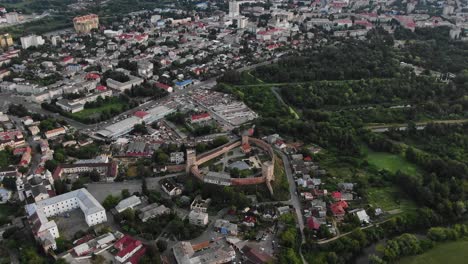 Luftaufnahme-Einer-Stadt-Mit-Mittelalterlicher-Festung,-Umgeben-Von-Gebäuden-Und-Wäldern-In-Osteuropa