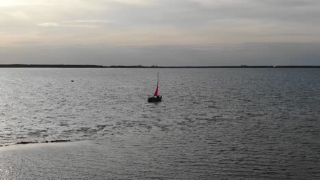 Luftaufnahme-Eines-Silhouettierten-Segelboots,-Das-Am-Frühen-Abend-Auf-Dem-Fluss-Vor-Anker-Liegt