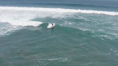 Vista-Aérea-Del-Surfista-Comienza-A-Surfear-En-Una-Ola-De-Luz-En-El-Océano-Pacífico