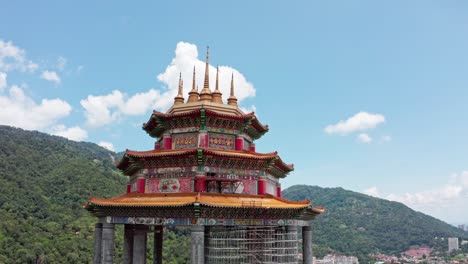 Panoramic-view-of-Kuan-Yin-Goddess-of-Mercy-statue-monument-in-Kek-Lok-Si-Buddhist-temple-with-city-background,-Aerial-drone-wide-orbit-reveal-shot